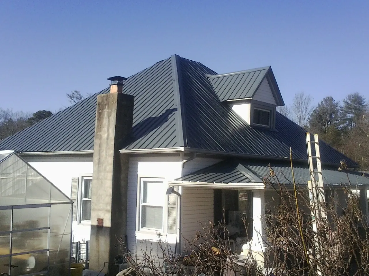 Dark blue standing seam metal roof on a white farmhouse with dormer — Slate & Tile Roof Repair by Roofing Brothers in Lake