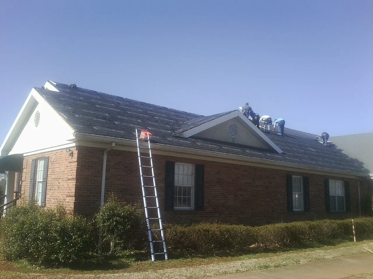 Crew tearing shingles off a brick ranch roof with a ladder set — Metal Roof Repair work by our crew in Lake