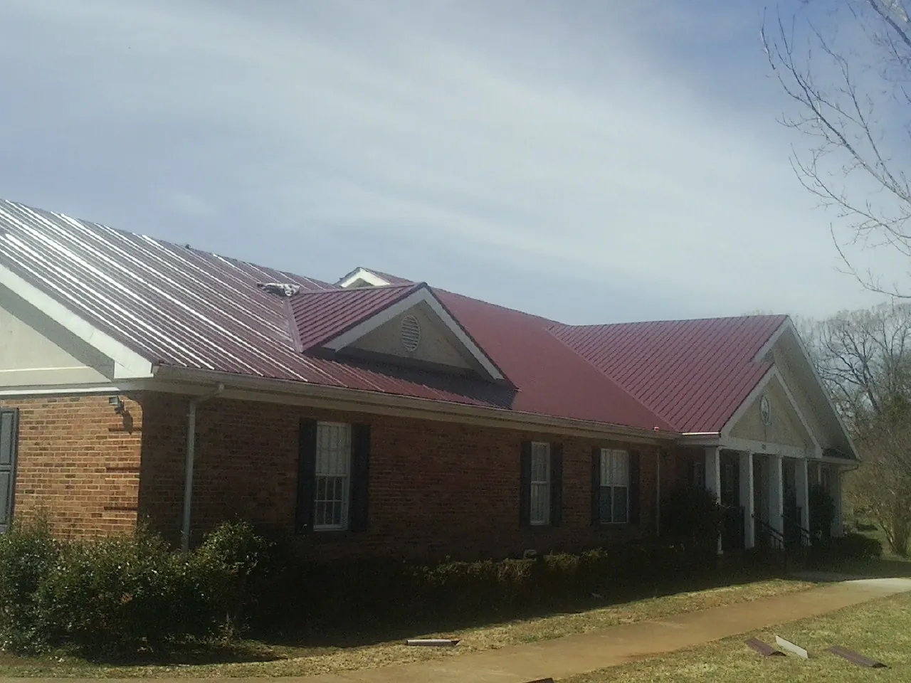 Red metal roof with gabled entries on a long brick building, from a Hail Damage Roof Repair job in Lake