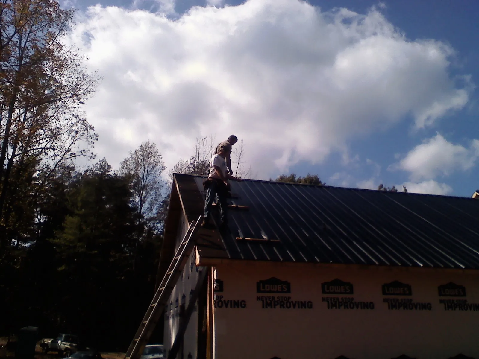 Roofer fastening dark metal panels high against a cloudy sky, from a Roof Inspection job in Lake