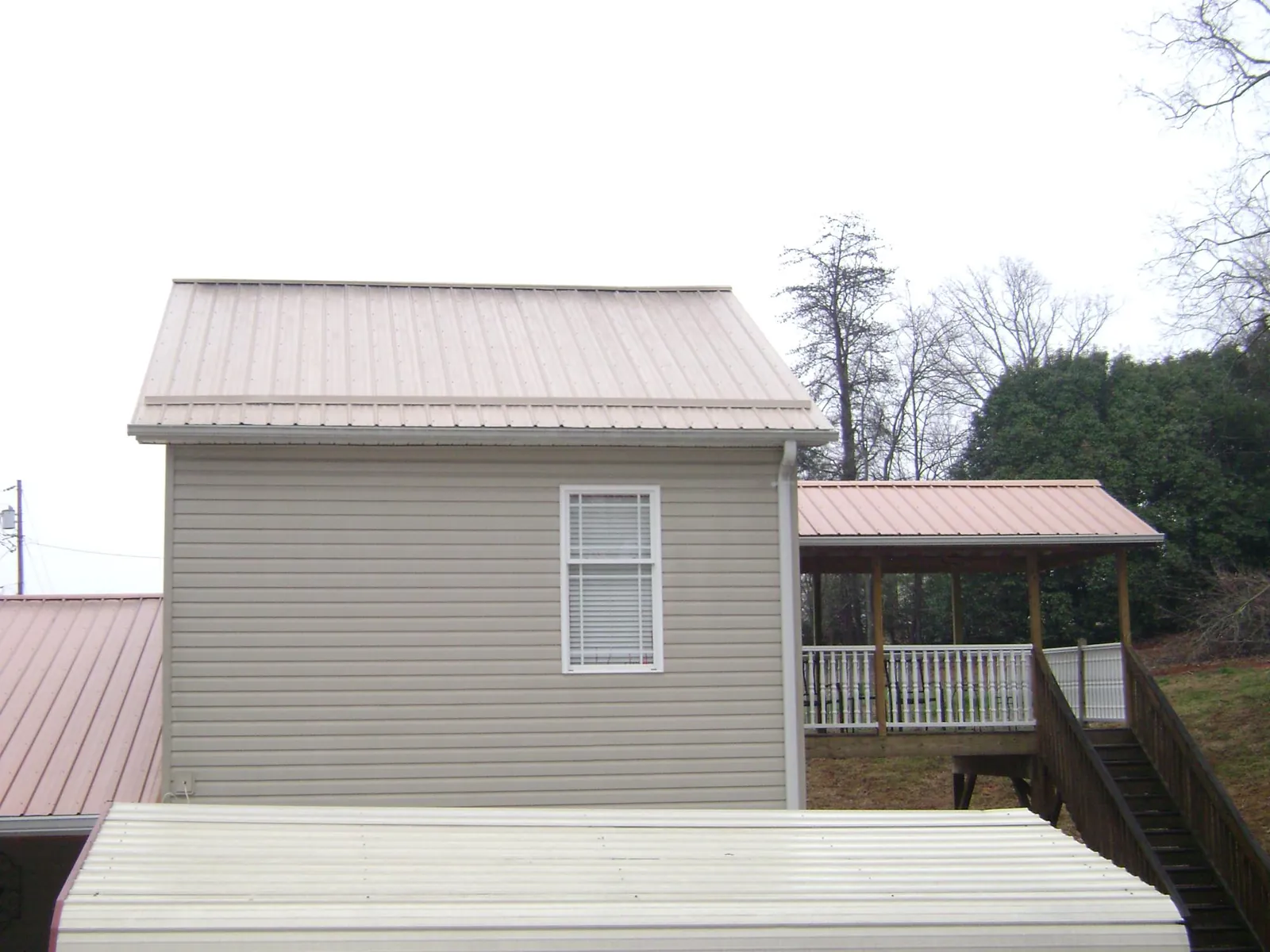 Tan metal roofs on a two story addition and attached porch, from a Roof Replacement job in Lake